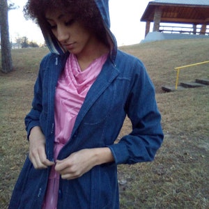 May include: A person wearing a blue denim jacket with a hood, a pink shirt, and a white stripe on the inside of the hood.