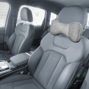May include: A gray car seat with a gray and green neck pillow. The pillow is shaped like a bow tie and has a textured fabric.