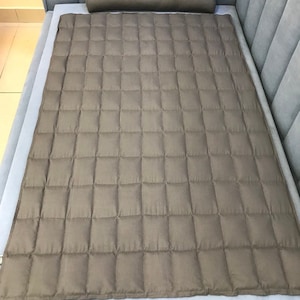 May include: A dark gray quilted bed topper with a matching cylindrical pillow. The topper has a square quilted pattern.