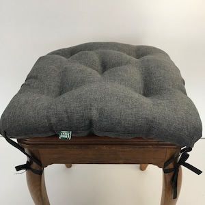 Puede incluir: Cojín de silla gris acolchado con lazos negros. El cojín está sobre una silla de madera con patas cabriole. El cojín tiene una etiqueta verde que dice "EKD Seat".