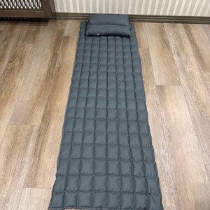 May include: A gray quilted sleeping mat with an attached pillow. The mat is rectangular with a grid pattern, and the pillow is a small, rectangular shape. The mat and pillow are made of a soft, padded material.