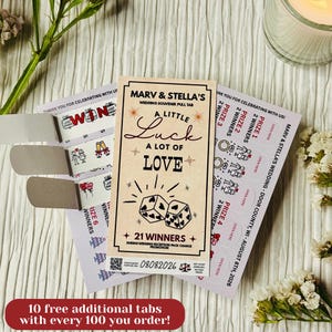 May include: A rectangular wedding pull tab game card with a beige background, featuring the text Marv & Stella's, A Little Luck A Lot Of Love, and 21 Winners. The design includes black dice with heart pips, stars, and a QR code at the bottom.