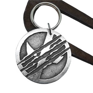 May include: Silver-toned metal keychain with a circular charm featuring a stylized rhino silhouette with a scratched design. The keychain is attached to a silver-toned metal ring.