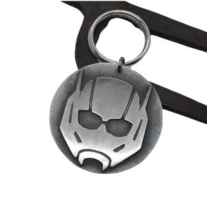 May include: A silver-colored round keychain featuring the Ant-Man helmet design. The keychain is attached to a silver key ring. The background is white.