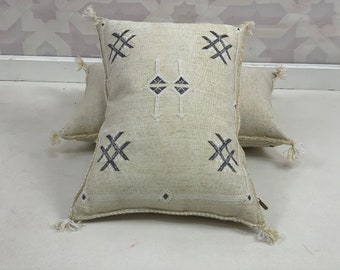 Puede incluir: Dos almohadas de color blanco roto con bordados geométricos en blanco y negro. Las almohadas tienen borlas en las esquinas.