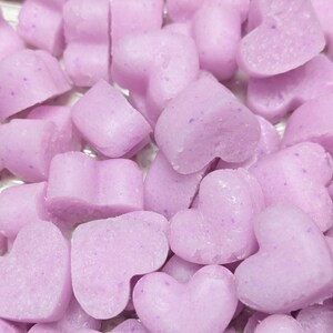 May include: A close-up shot of a pile of light purple heart-shaped objects. The objects have a slightly textured surface and appear to be small, possibly candies or soaps. The color is a soft, pastel lavender.