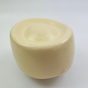 May include: A cream-colored, round, ceramic bowl with a slightly raised center. The bowl has a smooth, matte finish.