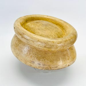 Könnte beinhalten: Eine vintage, cremefarbene, hölzerne Hutform mit abgerundetem Oberteil und einem breiten, ausgestellten Boden. Die Form ist aus glattem, hellem Holz gefertigt und hat eine leicht strukturierte Oberfläche.