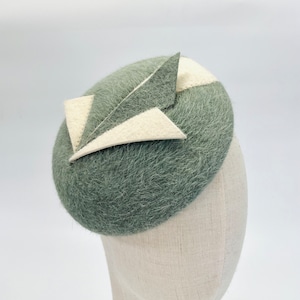 May include: A green felt hat with a white and green geometric design. The hat is on a white mannequin head.