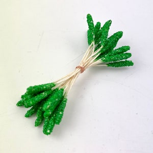 Peut inclure: Un bouquet de tiges florales vertes et scintillantes avec des tiges de fil blanc. Les tiges sont liées ensemble avec un fil de cuivre.
