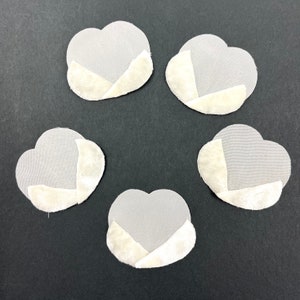 May include: Five grey fabric flower petals with white felt backing. The petals are arranged in a circle on a black surface.