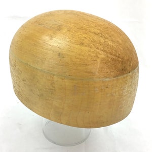 Könnte beinhalten: Eine hellbraune Hutform aus Holz, die zum Herstellen von Hüten verwendet wird, wird auf einem durchsichtigen Glasständer präsentiert.