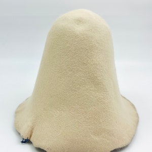 Puede incluir: Un sombrero de fieltro de color crema con un ala ancha y una corona redondeada. El sombrero está hecho de un material suave y peludo.