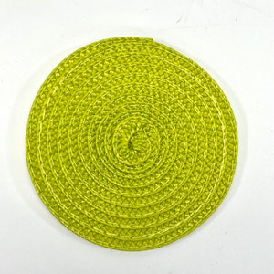 May include: A round, green woven placemat with a concentric circle design. The placemat is made of a natural material and has a subtle sheen.