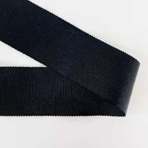 Könnte beinhalten: Nahaufnahme eines marineblauen Ripsbandes. Das Band hat eine gerippte Textur und einen gewellten Rand. Es ist diagonal vor einem weißen Hintergrund angeordnet.