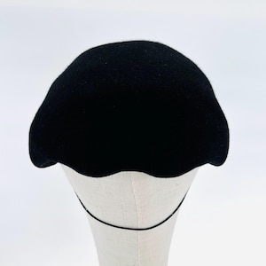 Könnte beinhalten: Ein schwarzer Filzhut im Cloche-Stil mit abgerundeter Krone und einem gewellten Rand. Der Hut wird auf einem weißen Mannequin-Kopf präsentiert.