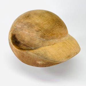 Könnte beinhalten: Baseballkappe aus Holz mit gebogenem Schirm. Die Kappe besteht aus hellbraunem Holz und hat eine glatte, polierte Oberfläche. Die Kappe hat eine kugelförmige Form mit einem Visier.