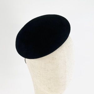 May include: A black felt hat with a rounded, oval crown. The hat is displayed on a mannequin head, highlighting its shape and design. The hat's dark colour and simple design suggest a classic, elegant style, suitable for formal occasions.