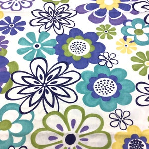Pode incluir: Um tecido branco com um padrão repetitivo de flores coloridas. As flores são em tons de azul, verde, roxo e amarelo. As flores são estilizadas e têm um aspeto retro.