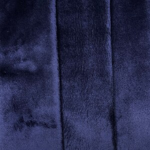 May include: Close-up of a dark blue fabric with a soft, fuzzy texture. The fabric has a subtle sheen and appears to be made of a plush material.