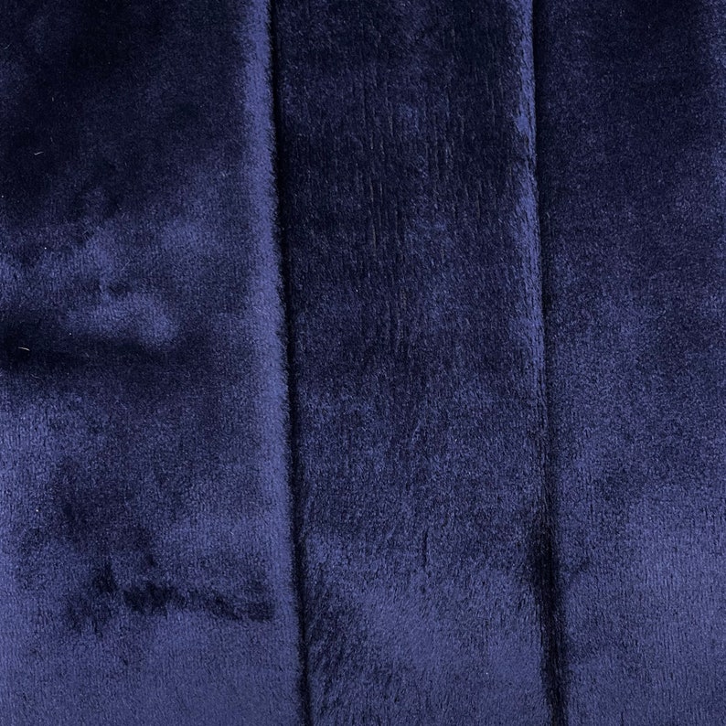 May include: Close-up of a dark blue fabric with a soft, fuzzy texture. The fabric has a subtle sheen and appears to be made of a plush material.