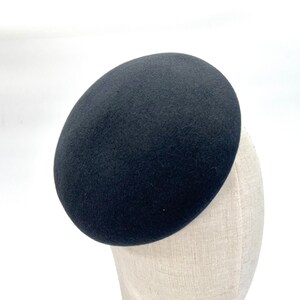 Può includere: Un cappello a pillola in feltro nero. Il cappello è rotondo e ha una superficie liscia.