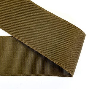 Könnte beinhalten: Ein braunes Grosgrainband mit einer strukturierten Oberfläche. Das Band ist in der Mitte gefaltet und die Kanten sind sichtbar.
