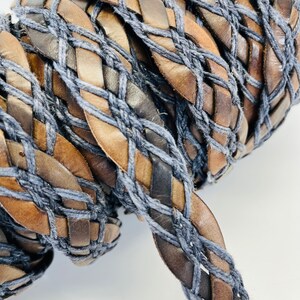 Könnte beinhalten: Nahaufnahme eines geflochtenen Kordels aus braunem Leder und blauer Baumwolle. Das Kordel ist in einem komplexen Muster gewebt, wodurch ein strukturiertes und optisch ansprechendes Design entsteht.