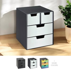 May include: A dark grey desktop organiser with four drawers and a top compartment. The drawer fronts are a brushed silver colour, and the handles are cut-out style. The organiser is on a light wood surface.