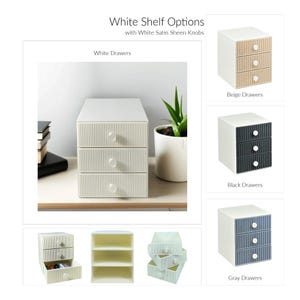 May include: A white three-drawer storage unit with white satin sheen knobs. The image also shows options with beige, black, and gray drawers. The text reads "White Shelf Options with White Satin Sheen Knobs."