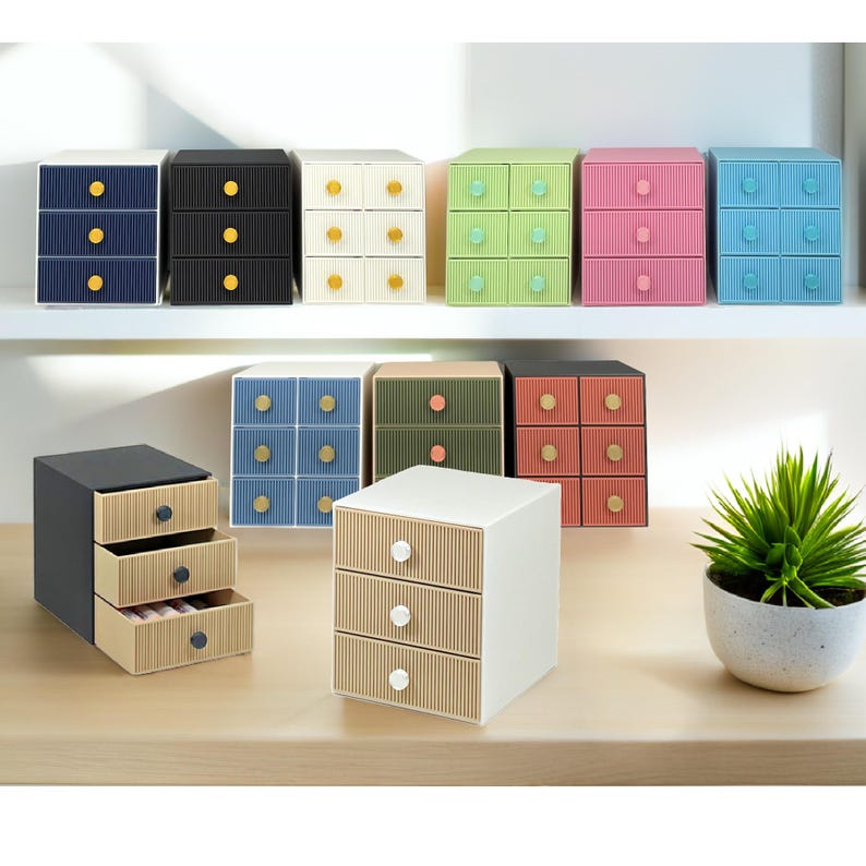 May include: A collection of small, colorful storage drawers with three or six compartments. The drawers are in various colors, including blue, black, white, green, pink, and beige. Each drawer has a contrasting colored knob. A small potted plant is also visible.