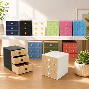 Op de afbeelding: Een verzameling kleine, kleurrijke opberglades. De laden zijn gerangschikt in verschillende kleuren, waaronder blauw, zwart, wit, groen, roze en rood. Elke lade heeft drie uittrekbare laden met een contrasterende knop.