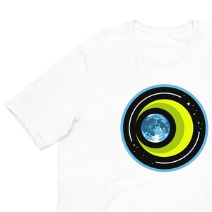 Könnte beinhalten: Weißes T-Shirt mit einem Motiv einer blauen und grünen Erde, umgeben von einem gelben Halbmond und schwarzen Ringen auf schwarzem Hintergrund.