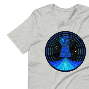 May include: A grey t-shirt with a blue and black circular graphic of a spaceship in space. The spaceship is surrounded by concentric circles and stars.
