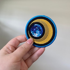Könnte beinhalten: Ein gestickter Aufnäher in Blau und Gold mit einem Halbmond und einem blauen und weißen Globus darin.