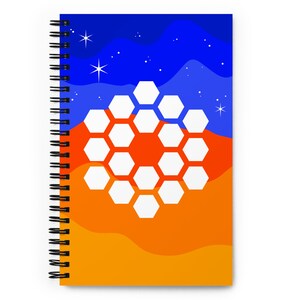 Op de afbeelding: Een spiraalgebonden notitieboek met een kleurrijk abstract ontwerp. De omslag heeft een wit honingraatpatroon op een gradiënt achtergrond van oranje en blauw met witte sterren.