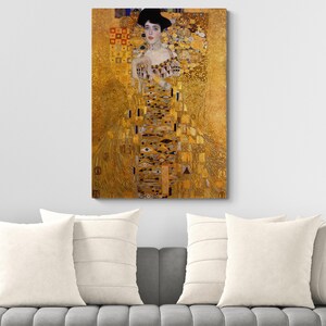 May include: A rectangular wall art print featuring a portrait of a person in a gold-toned dress with intricate geometric patterns, including eye motifs and squares, set against a shimmering gold background with dark hair and a choker necklace.