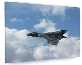 May include: A gray and green camouflage military jet plane flies in a blue sky with white clouds. The plane has a red, white, and blue roundel on the wing.
