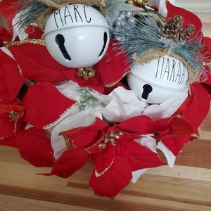 May include: A Christmas wreath with red poinsettia flowers and two white bells with the names "Marc" and "Marah" written on them.