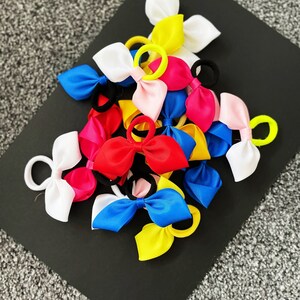 May include: A collection of colorful hair bows with elastic bands. The bows are made of satin ribbon and come in a variety of colors, including red, pink, blue, yellow, and white.