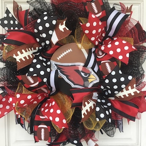 May include: A red, white and black football wreath featuring a Cardinals logo. The wreath is decorated with polka dot ribbon, football-patterned ribbon and black and white striped ribbon.