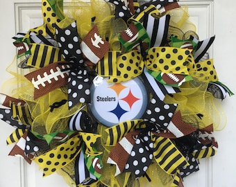 Könnte beinhalten: Ein gelber, schwarzer und weißer Pittsburgh Steelers Kranz mit einem schwarz-weißen Tupfenband, einem schwarz-gelben Streifenband und einem schwarz-weißen Streifenband mit einem Fußballmuster. Der Kranz hat in der Mitte ein Steelers-Logo.