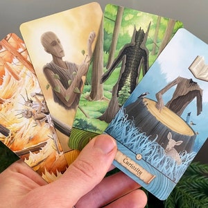 May include: Four tarot cards with illustrations of nature spirits. The cards are held in a hand. The card in the foreground is blue with a tree spirit with a book for a head. The text on the card reads "Curiosity".