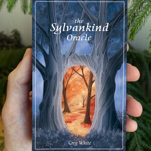 May include: The Sylvankind Oracle deck box features a blue and gray illustration of two trees with a forest scene visible through the opening between the trees. The text "the Sylvankind Oracle" is printed in white at the top of the box. The text "Greg White" is printed in white at the bottom of the box.