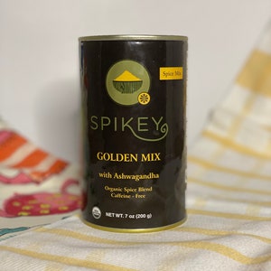 K&ouml;nnte beinhalten: Eine schwarze und goldene Dose SPIKEY GOLDEN MIX mit Ashwagandha, einem Bio-Gew&uuml;rz-Mix. Die Dose enth&auml;lt 200 Gramm (7 Unzen) und ist koffeinfrei.