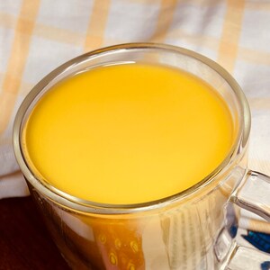 K&ouml;nnte beinhalten: Eine gl&auml;serne Tasse gef&uuml;llt mit einer leuchtend gelben Fl&uuml;ssigkeit, wahrscheinlich ein Getr&auml;nk wie Kurkuma-Milch oder goldene Milch.