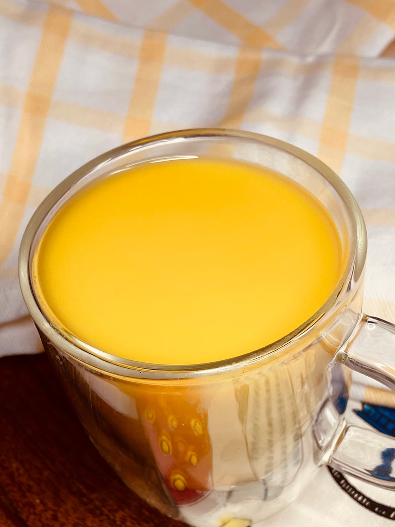 K&ouml;nnte beinhalten: Eine gl&auml;serne Tasse gef&uuml;llt mit einer leuchtend gelben Fl&uuml;ssigkeit, wahrscheinlich ein Getr&auml;nk wie Kurkuma-Milch oder goldene Milch.