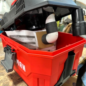 May include: A red and black handheld vacuum cleaner with a detachable dustbin. The vacuum cleaner is open and the dustbin is removed, revealing a white filter bag inside. The vacuum cleaner is sitting on a wooden surface.