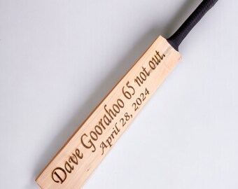 May include: A wooden cricket bat with a black handle. The bat is engraved with the text "Dave Gooraboo 65 not out, April 28, 2024".