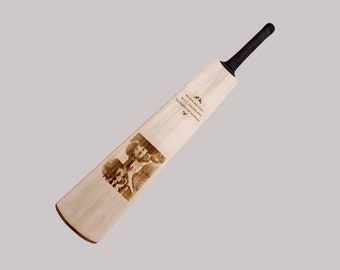 May include: A wooden cricket bat with a black handle and a personalized message engraved on the surface. The message includes a photo of two people and the text "Matthew John Brown, Born 14.08.2004, The sky's the limit for you, enjoy the journey".